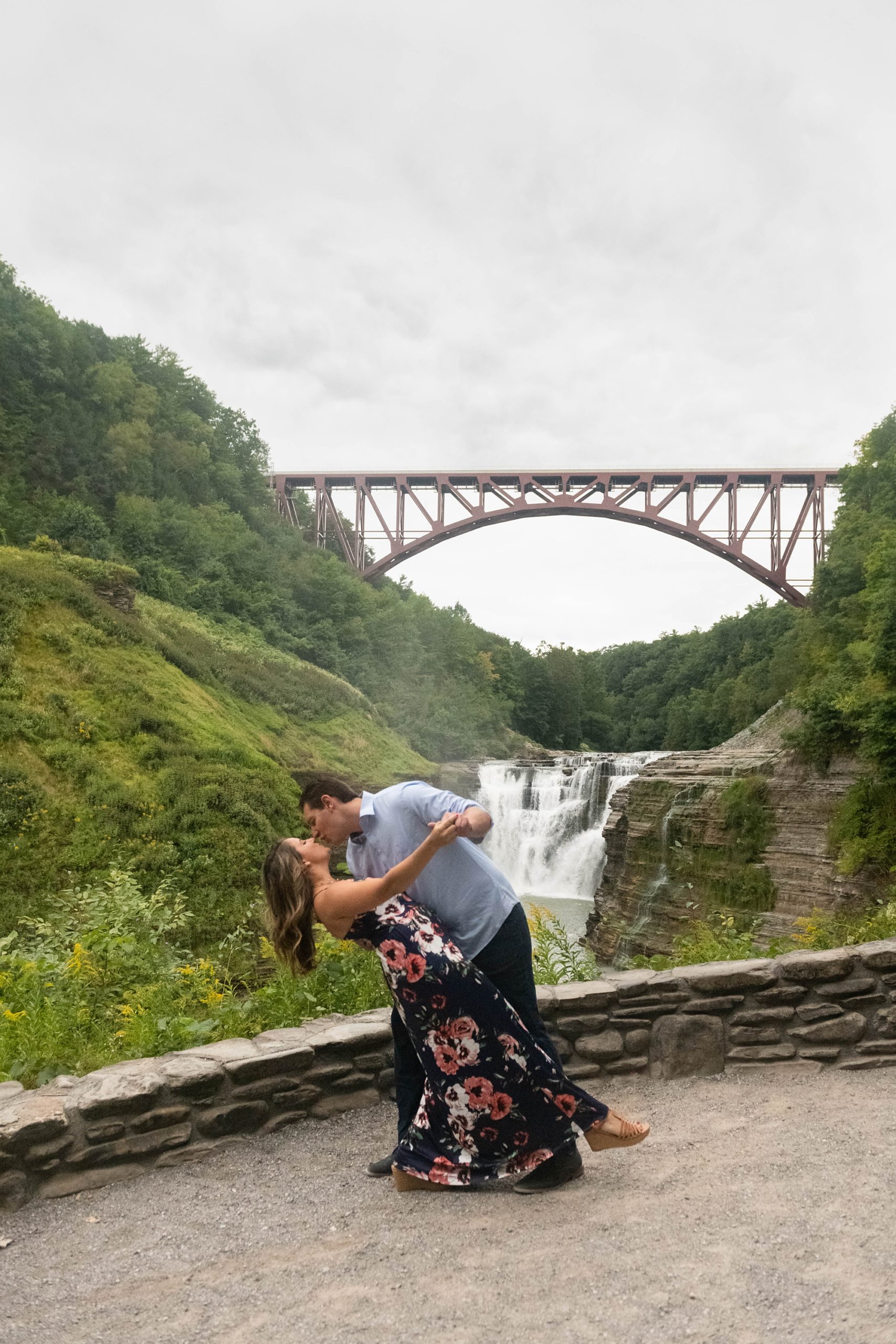 groom kisses bride and dips her in front of bridge