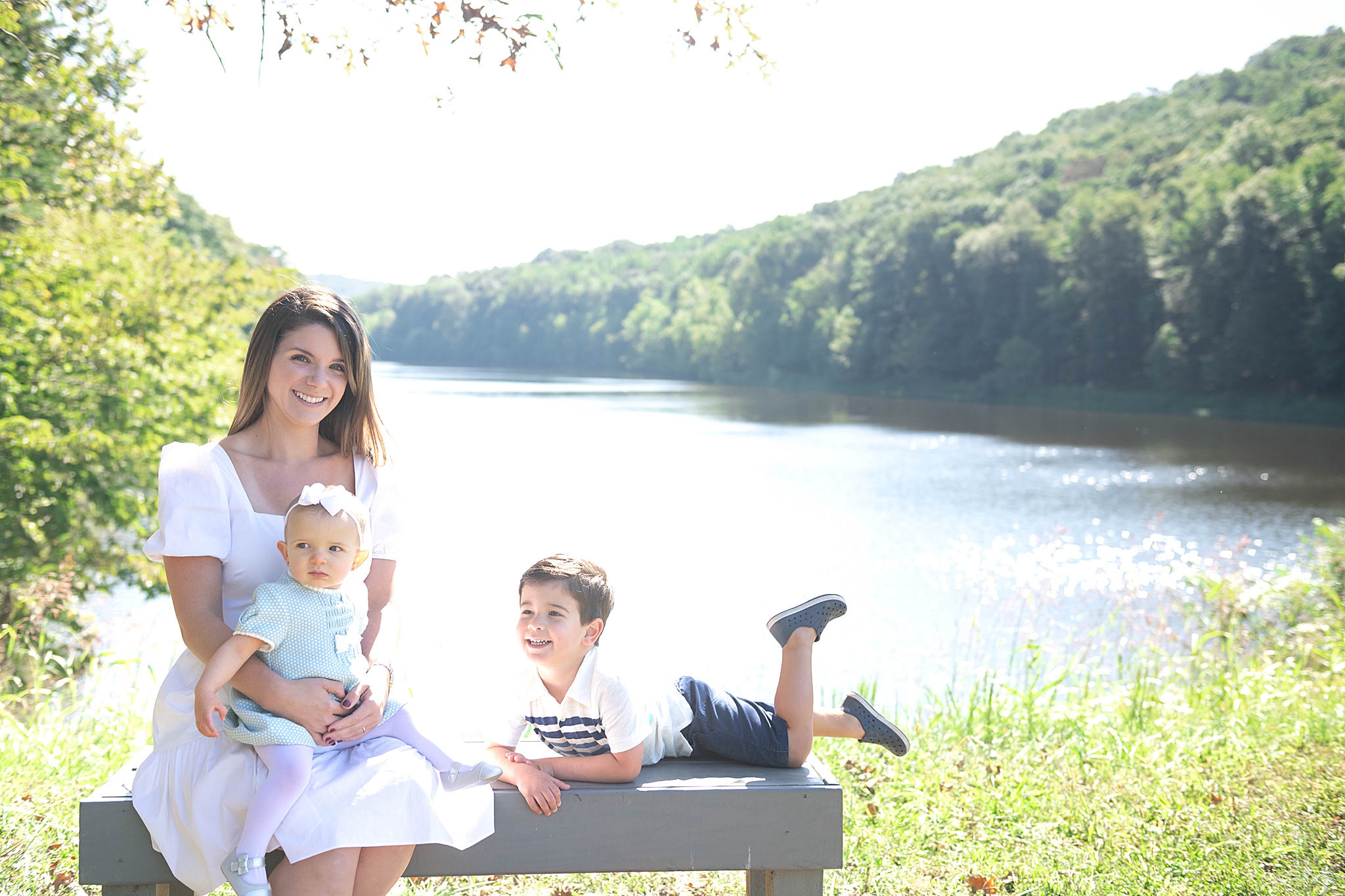mom poses with toddler on bench by lake