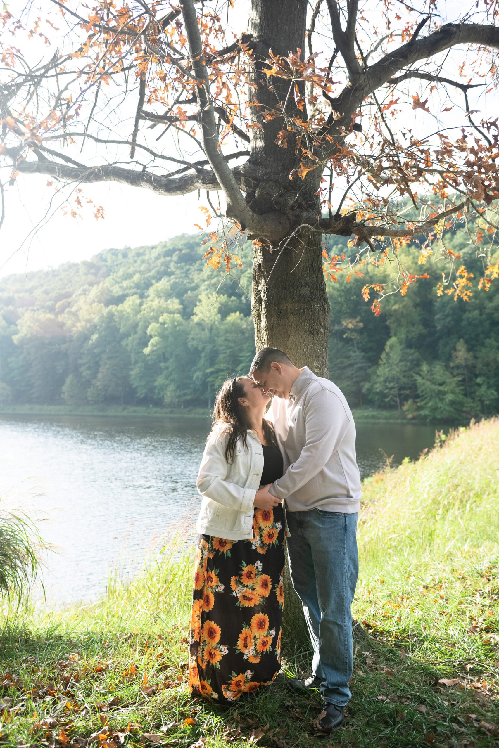 husband and wife kiss by tree along Lake Linganore