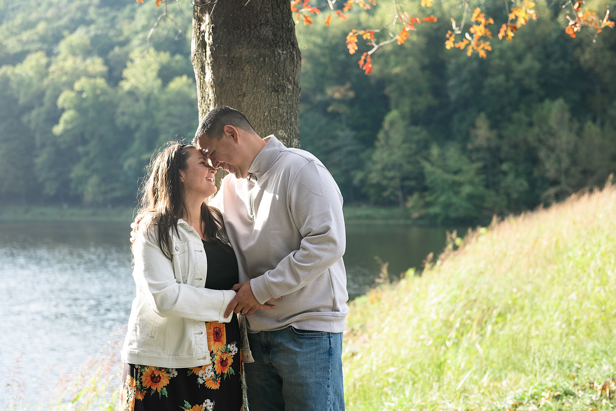 couple poses by trees during Fall maternity session in Lake Linganore
