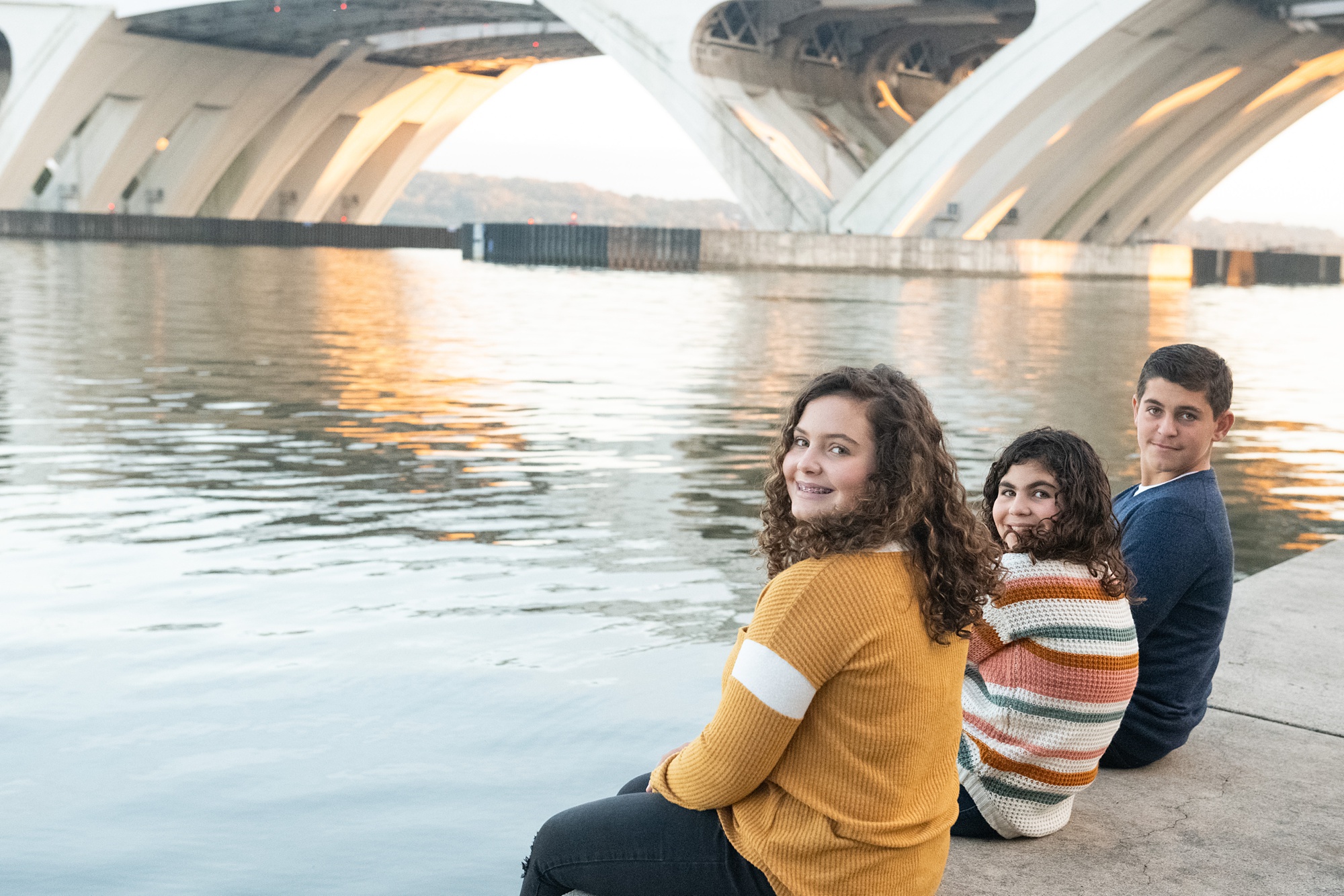 siblings sit along Potomac River during fall family photos